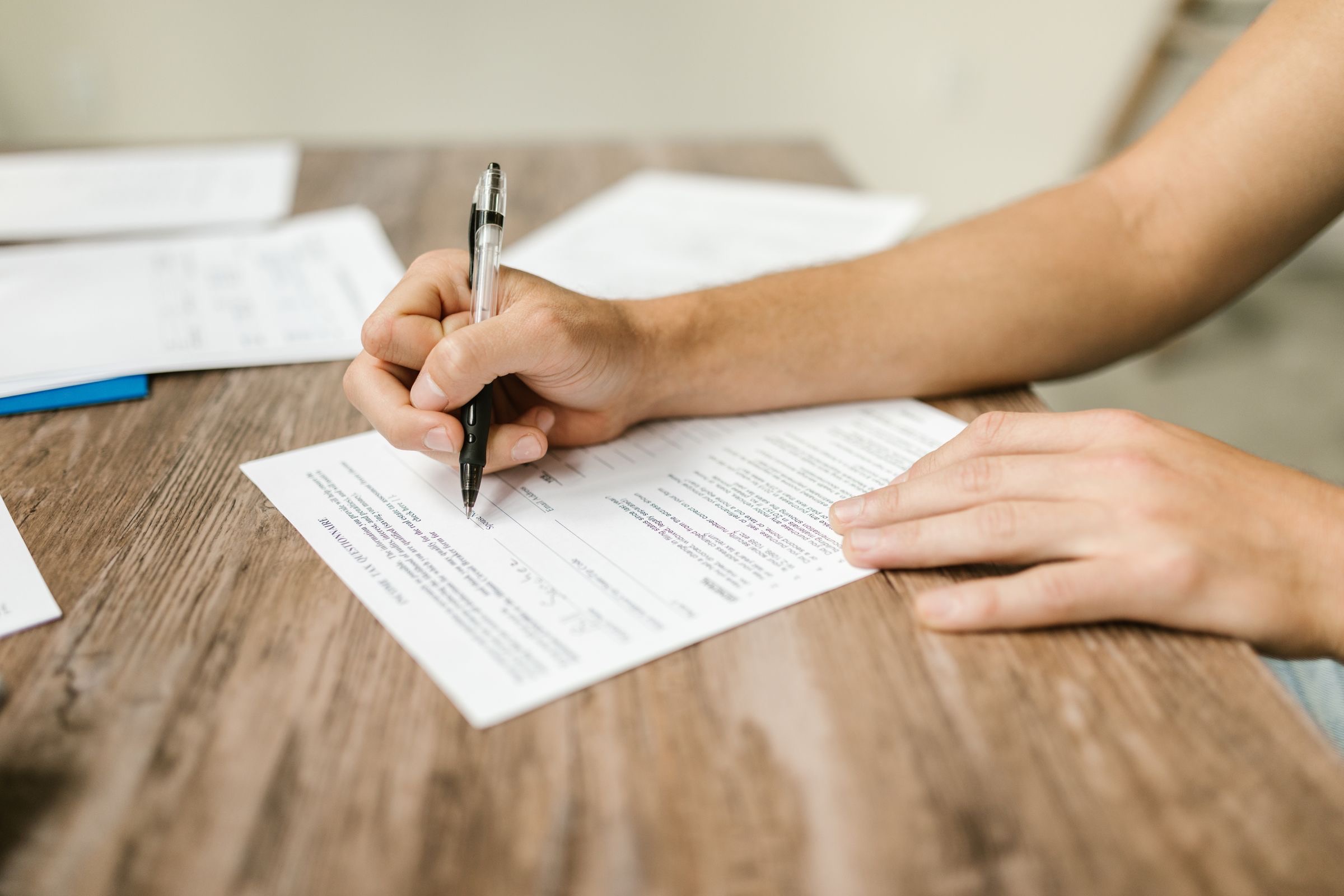 A hand signing a form at a desk beside a stamp and a laptop