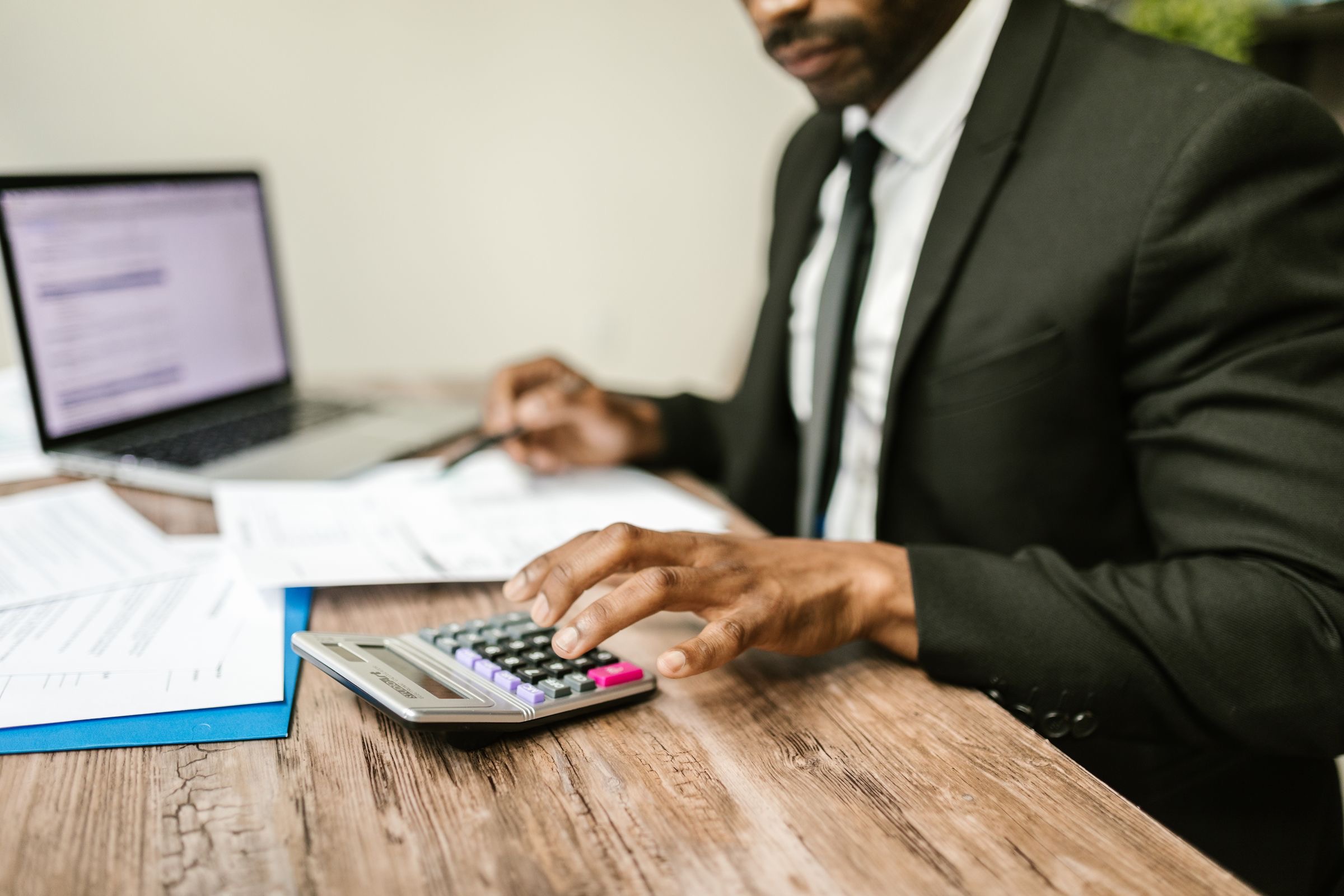 A man at a desk working with a calculator and a laptop
