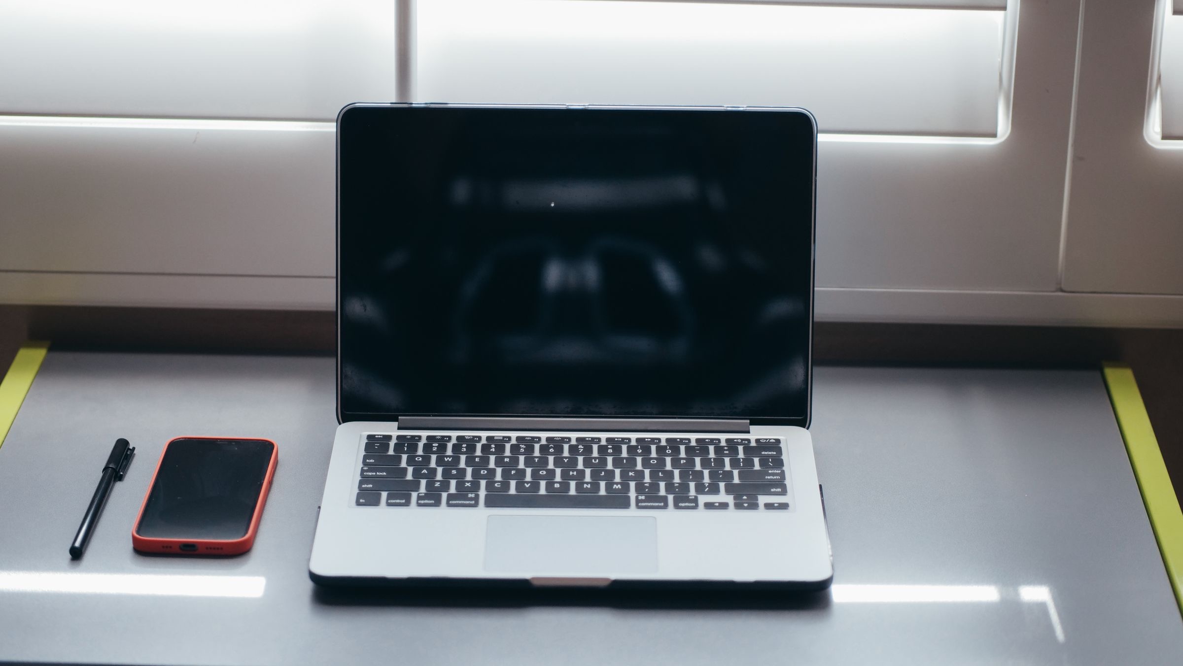 A laptop and a notebook on a table beside a shuttered window in an Italian apartment