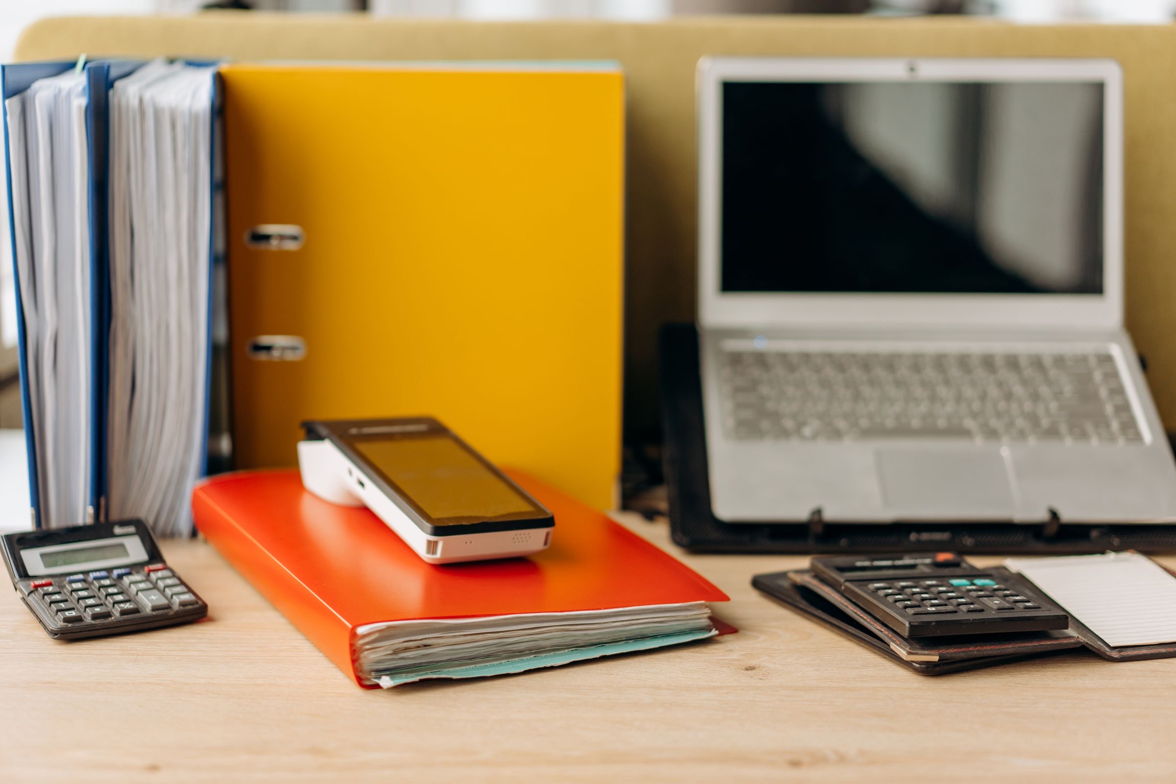 A desk with a ledger, a calculator and a laptop